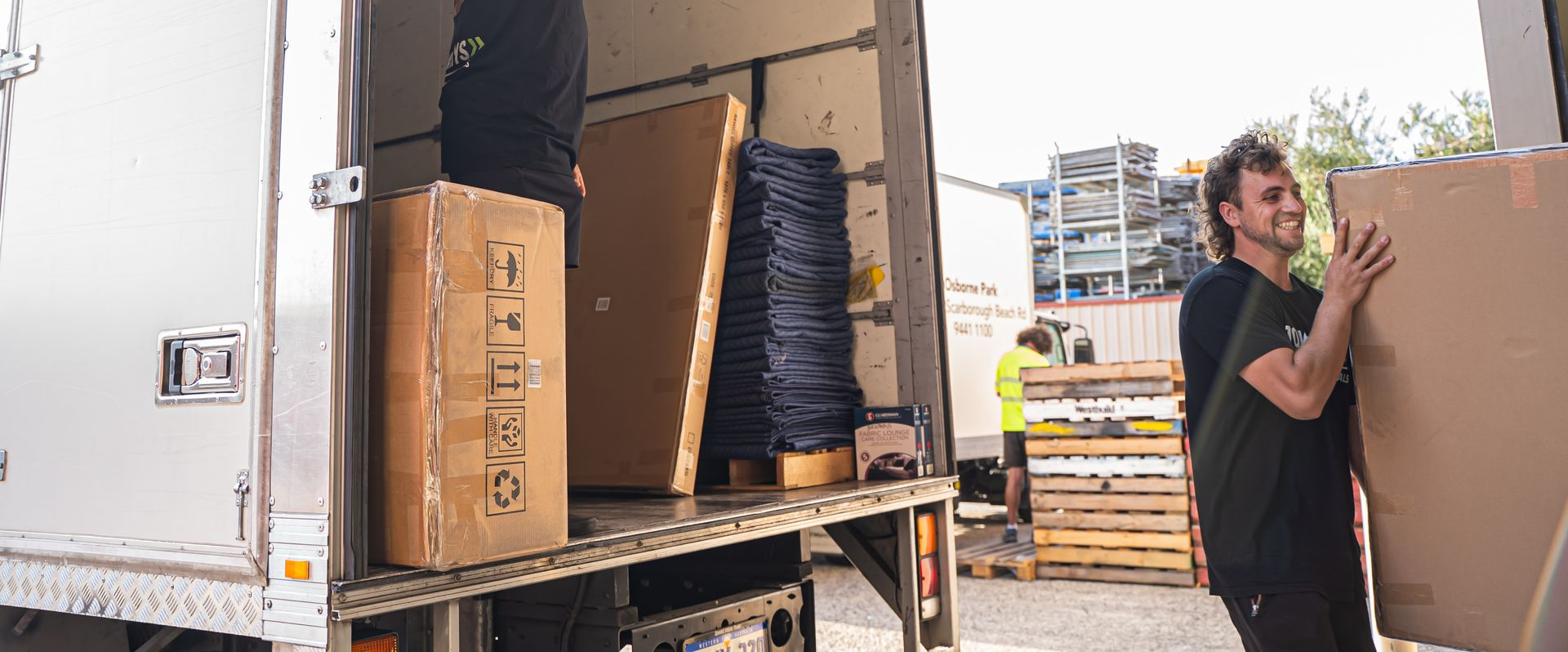 Two movers unloading large boxes from a truck at a warehouse dock.