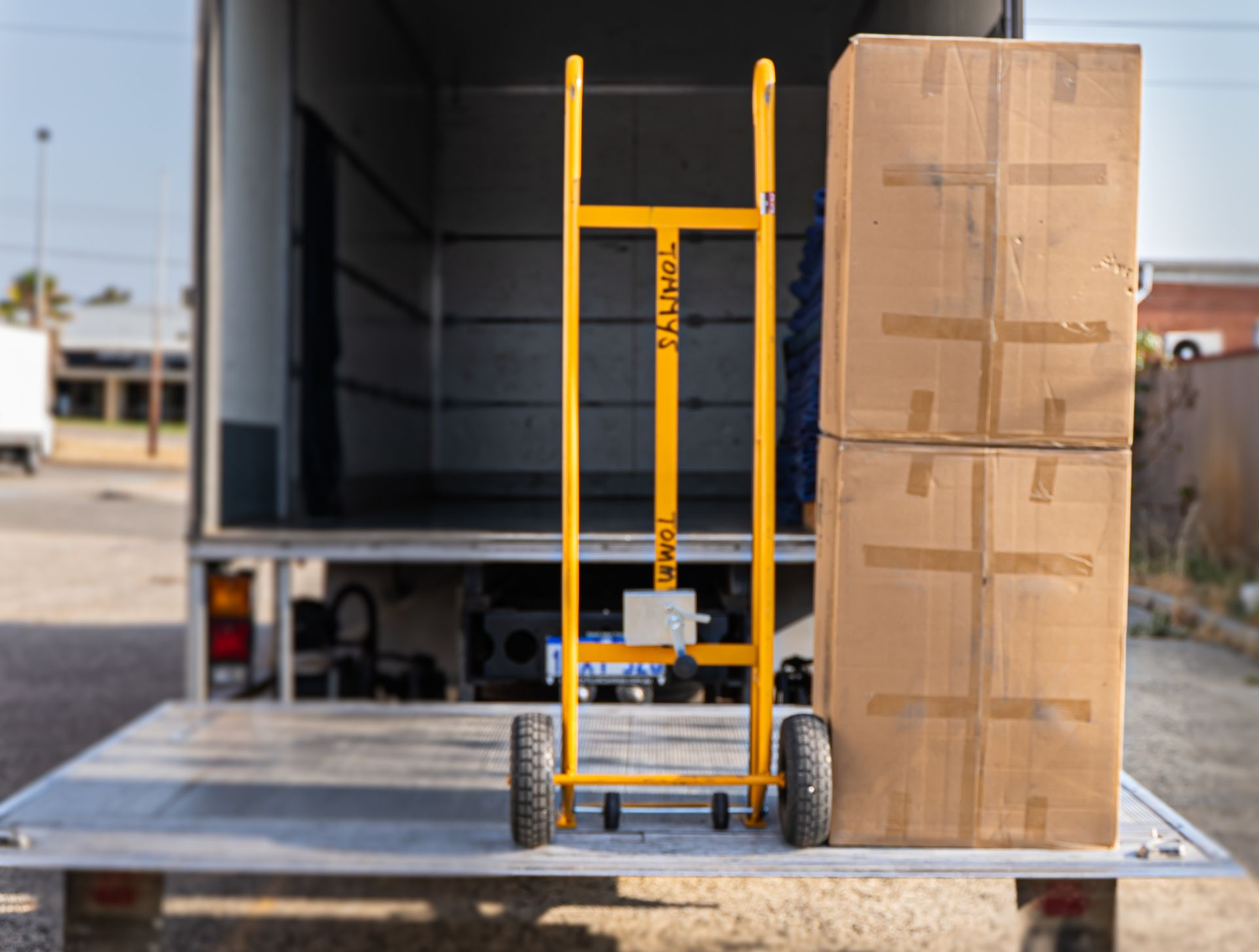 Yellow hand trolley beside stacked cardboard boxes on a flatbed removalist truck.