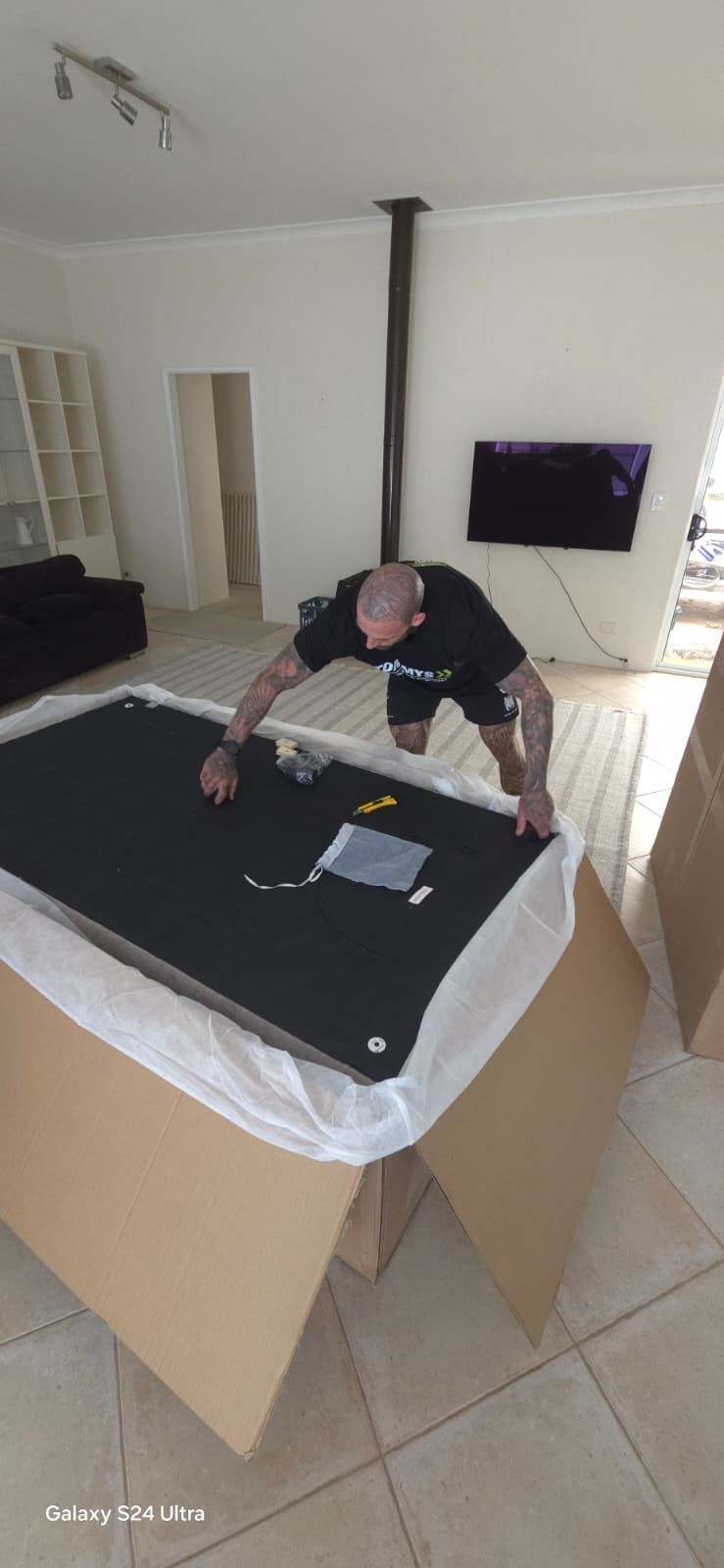 Tommy's Removalist team unwraps a new couch from cardboard packaging in a living room.