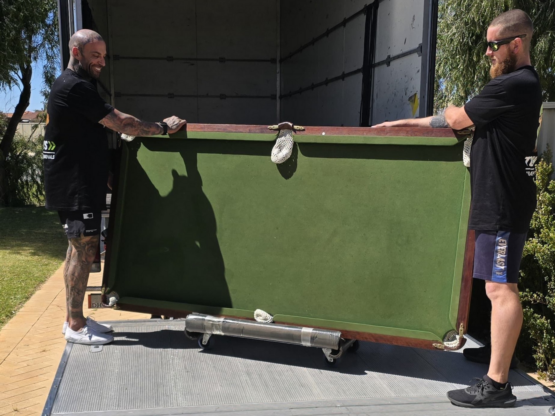 Two people lifting a large, green pool table into the moving truck in Perth