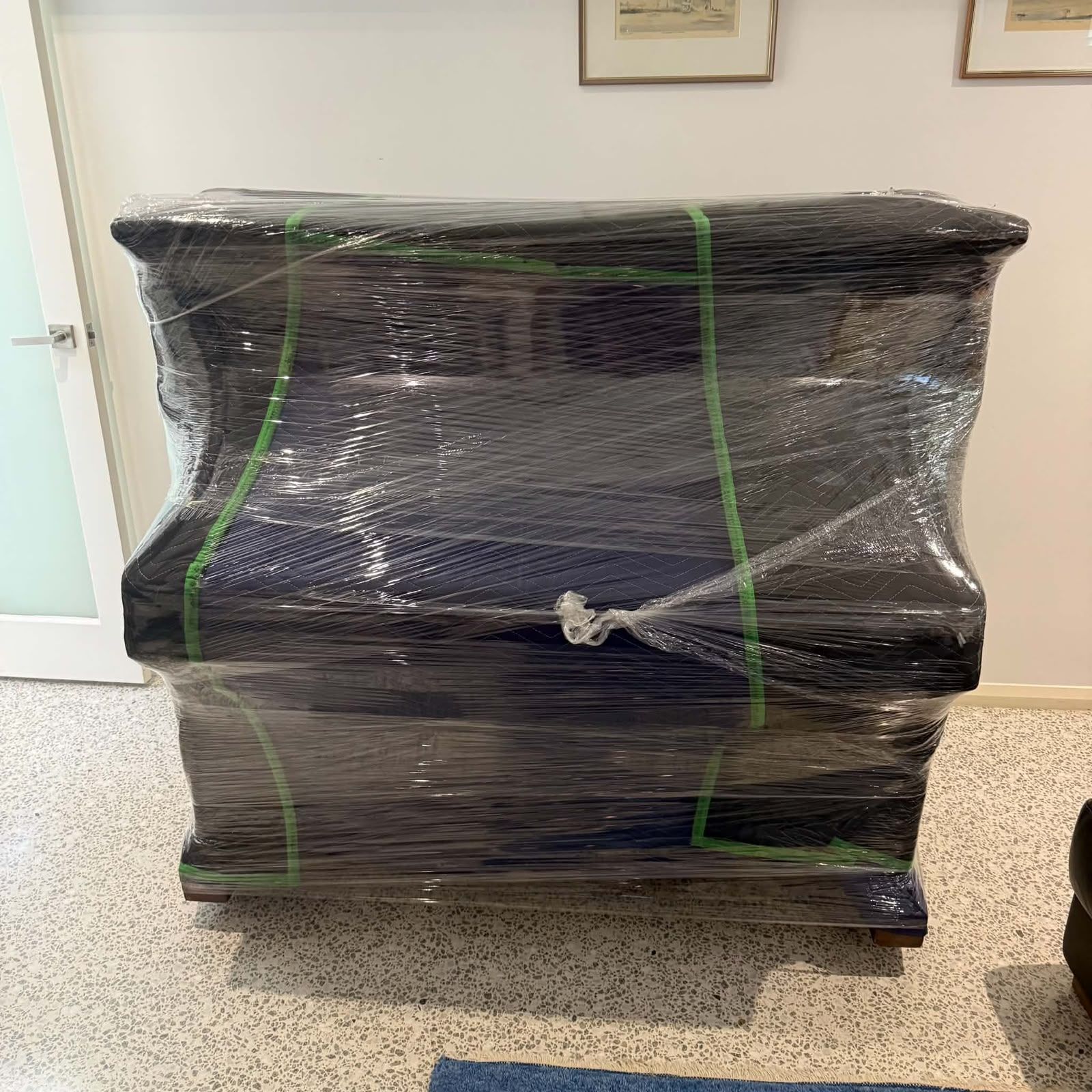 Black dresser wrapped in clear plastic stretch film, sitting indoors on a carpeted floor.