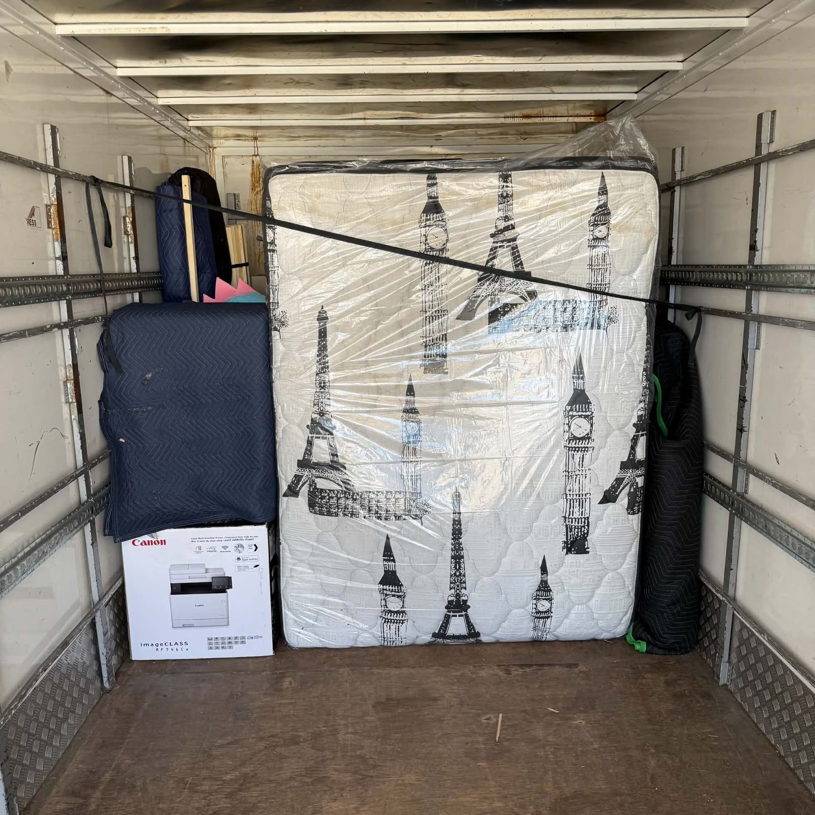 Packed moving truck with a wrapped mattress, boxes, and luggage inside.