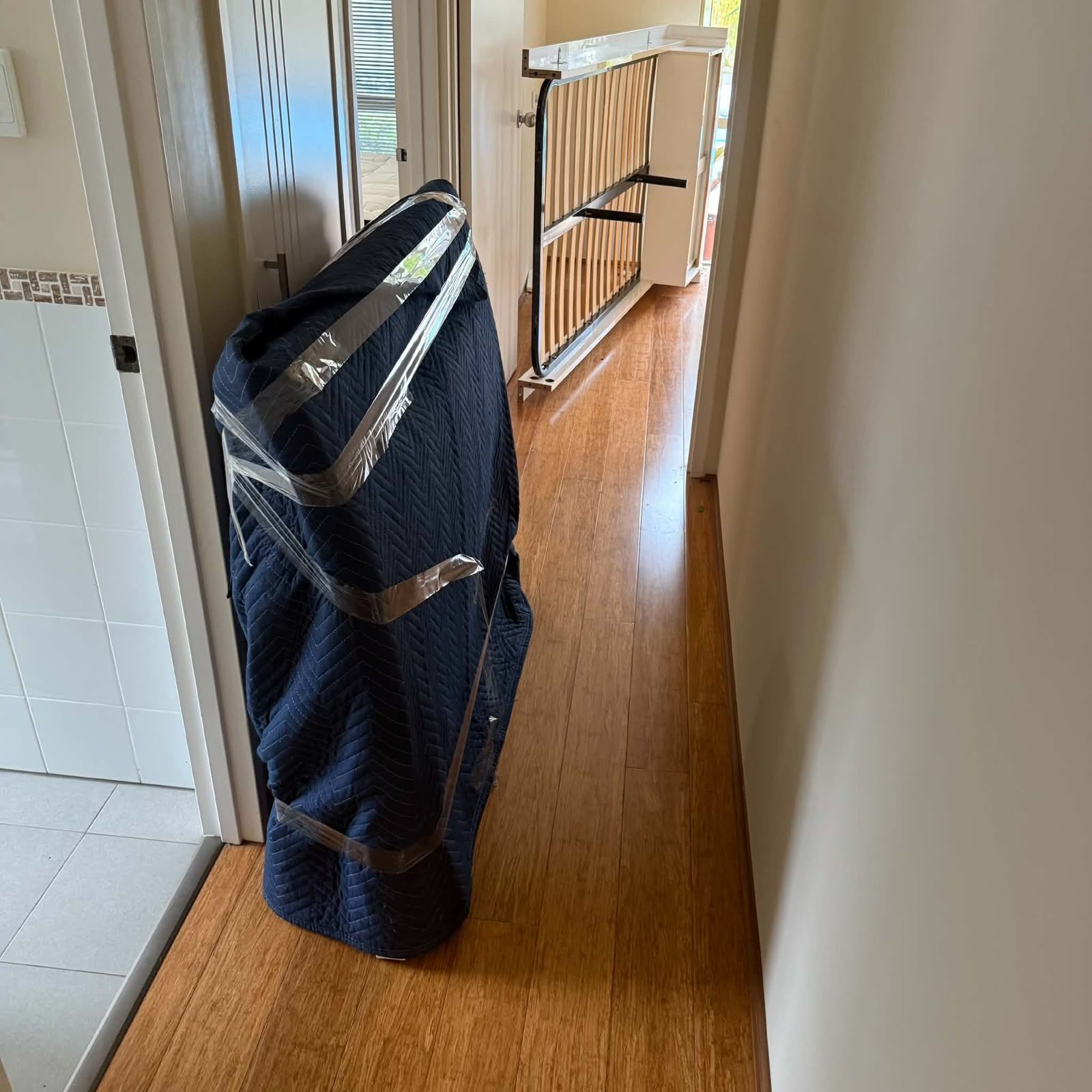 Tall navy wheeled bag in a narrow hallway beside a doorway and baby gate