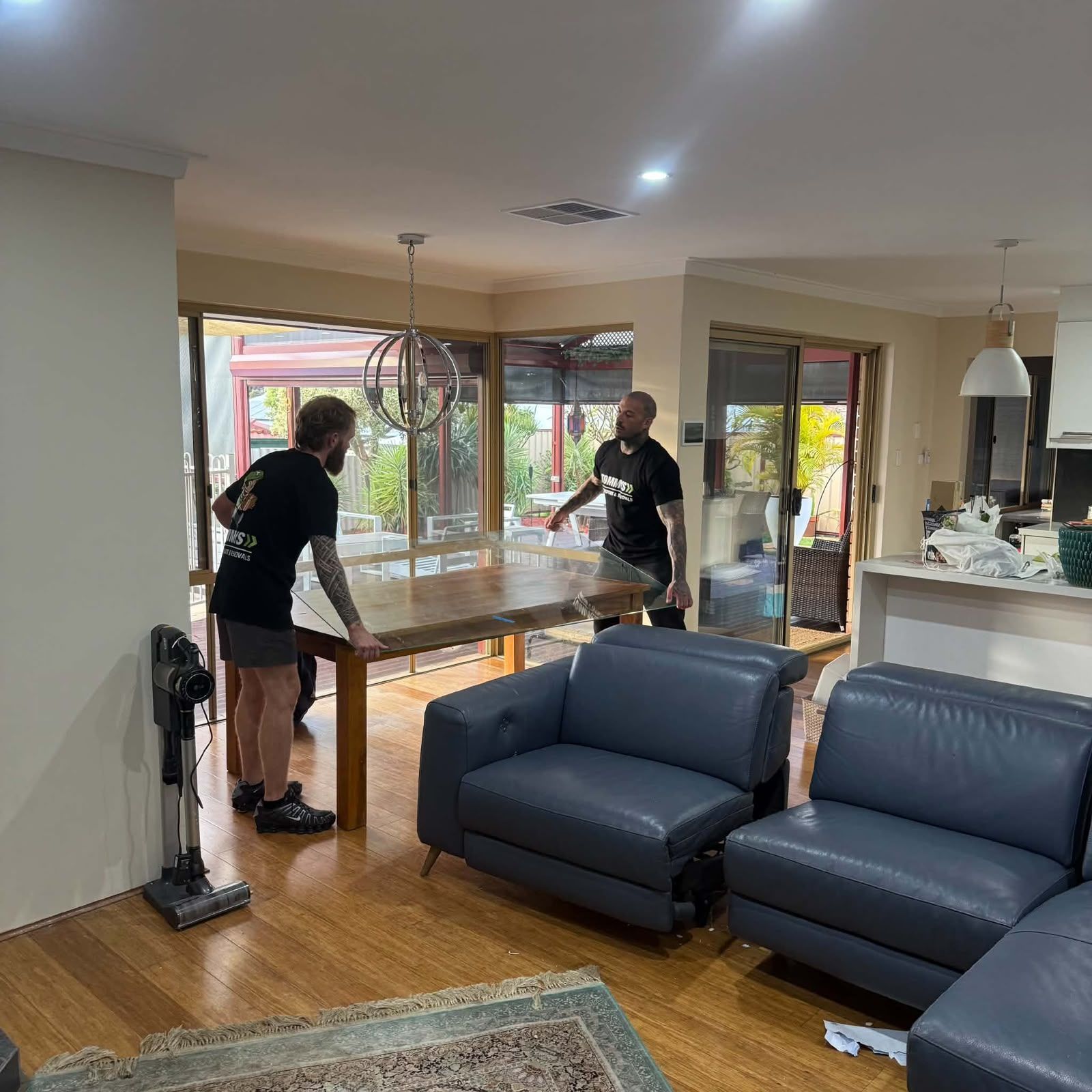 Two people moving a table in a bright living room with blue sofas and wood floors