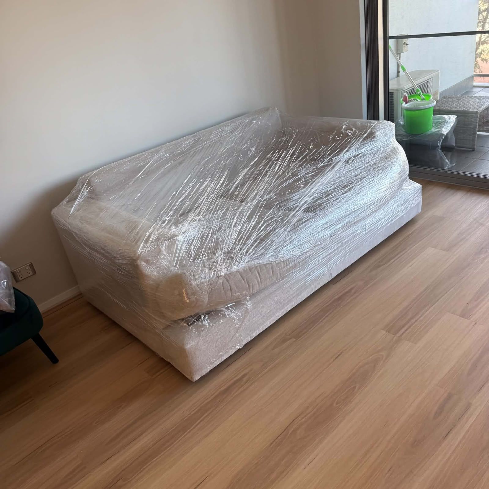 Wrapped mattress on the floor in a bright room near a window and balcony door