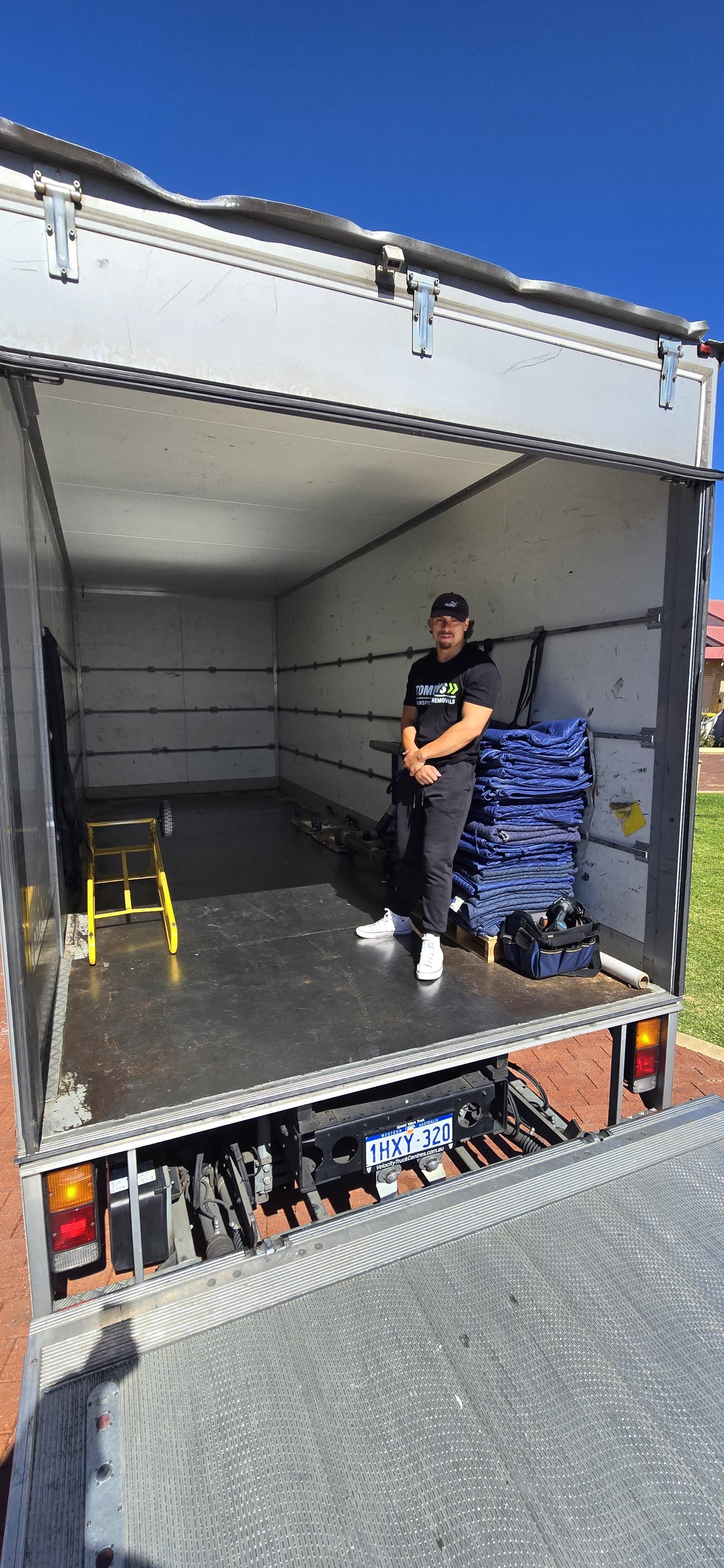 A person stands inside an empty moving truck, with stacked blue items on the side.