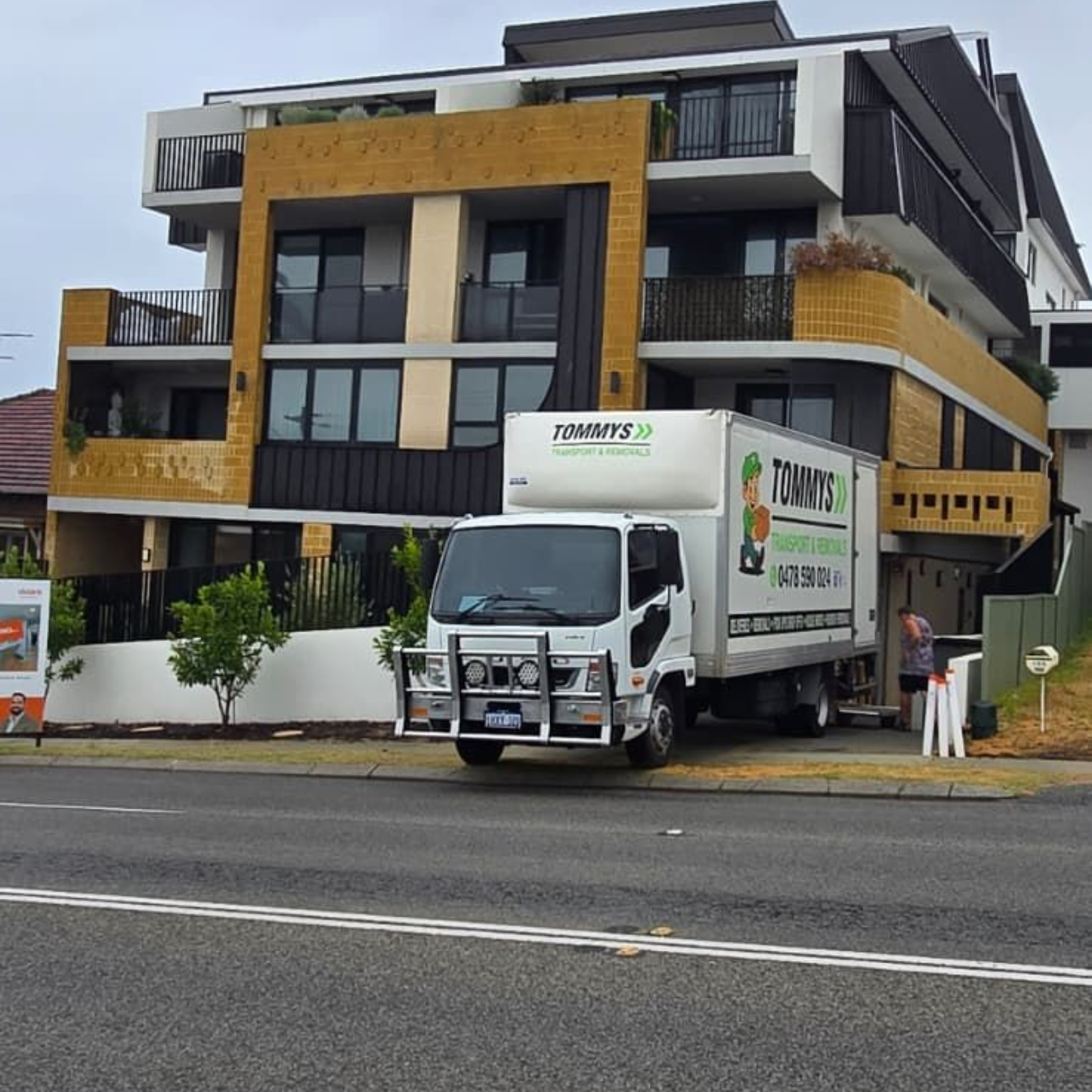 Modern multi-story building with yellow accents and a white delivery truck parked on the street.
