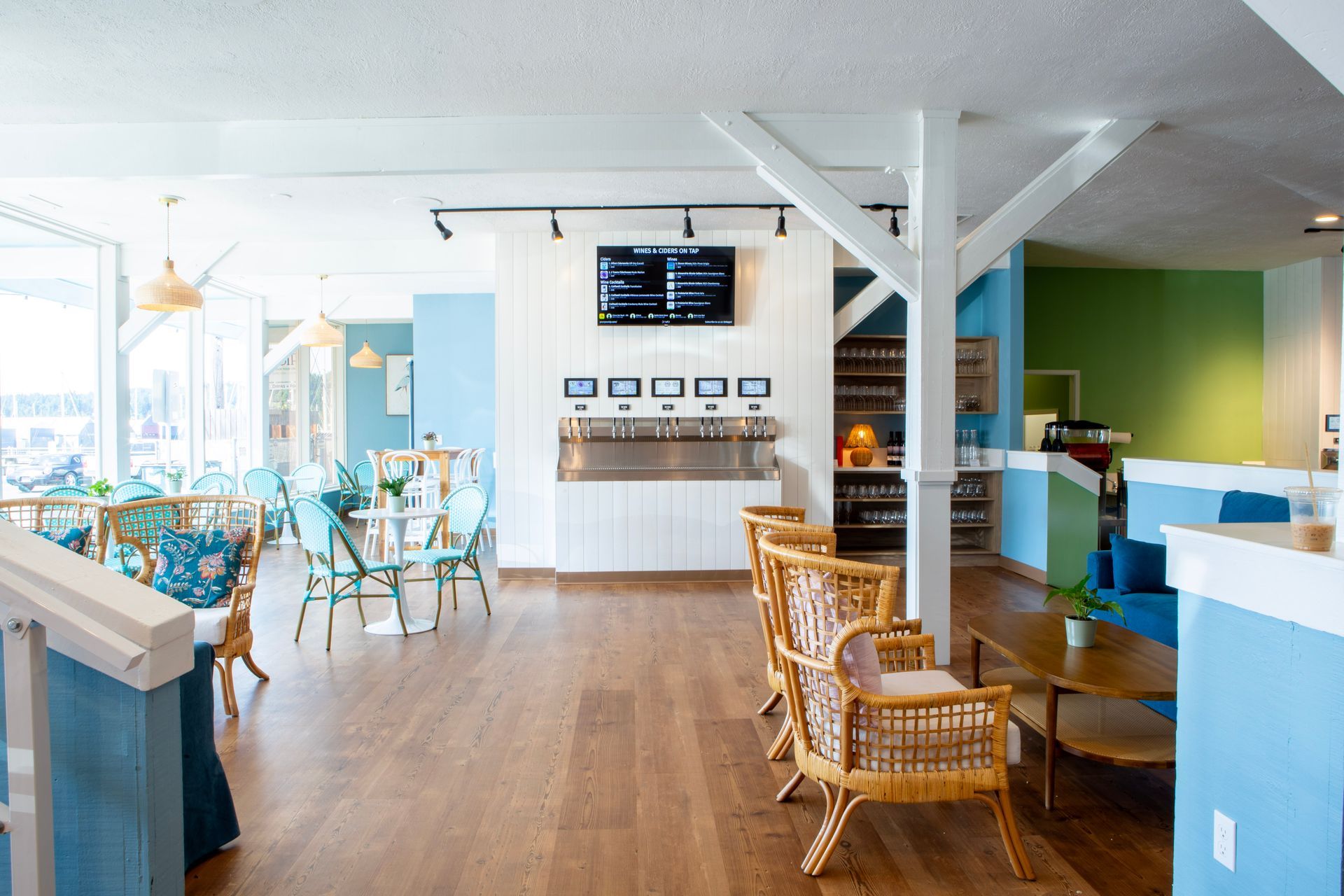 Bright cafe interior with wooden floors, blue and green walls, wicker furniture, and a bar.