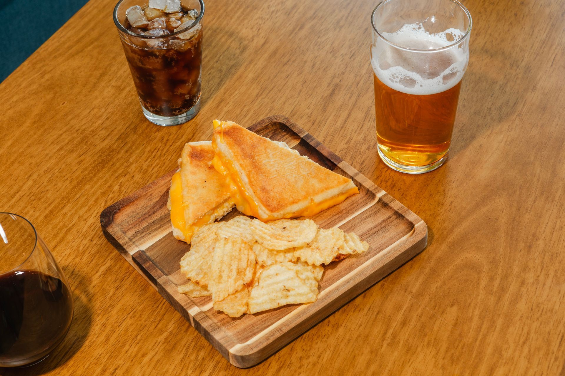 Grilled cheese sandwich and chips on a wooden tray, drinks on a table.