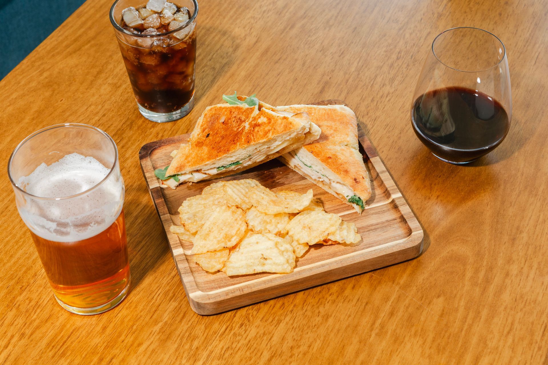 Sandwich, chips, beer, soda, and wine on wooden table.