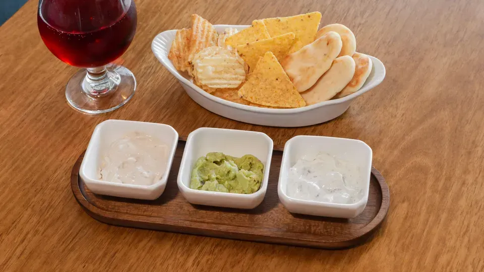 Chips, breadsticks, dips, and a glass of wine on a wooden table.
