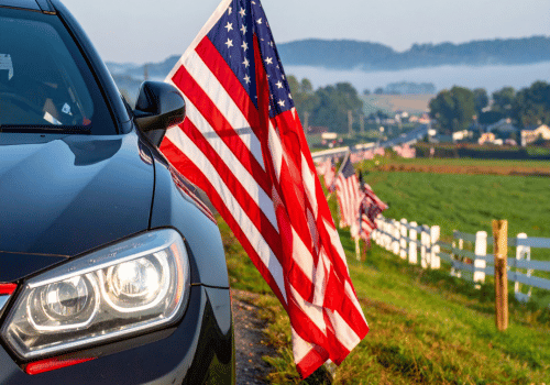 Close-up of a car parked beside American flags along a rural roadside.