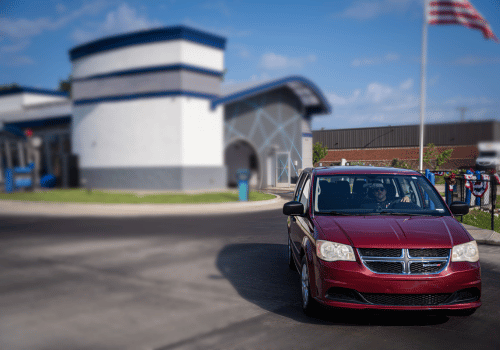 Red minivan arriving at a professional auto repair shop with a customer behind the wheel