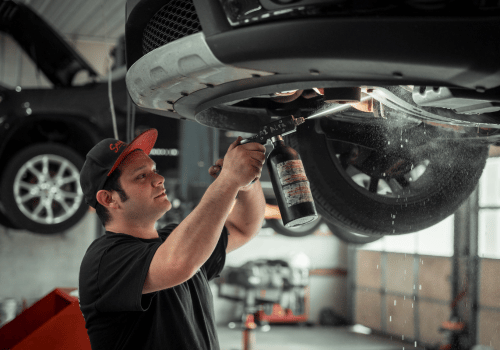 Technician applying a protective underbody treatment to a vehicle on a lift