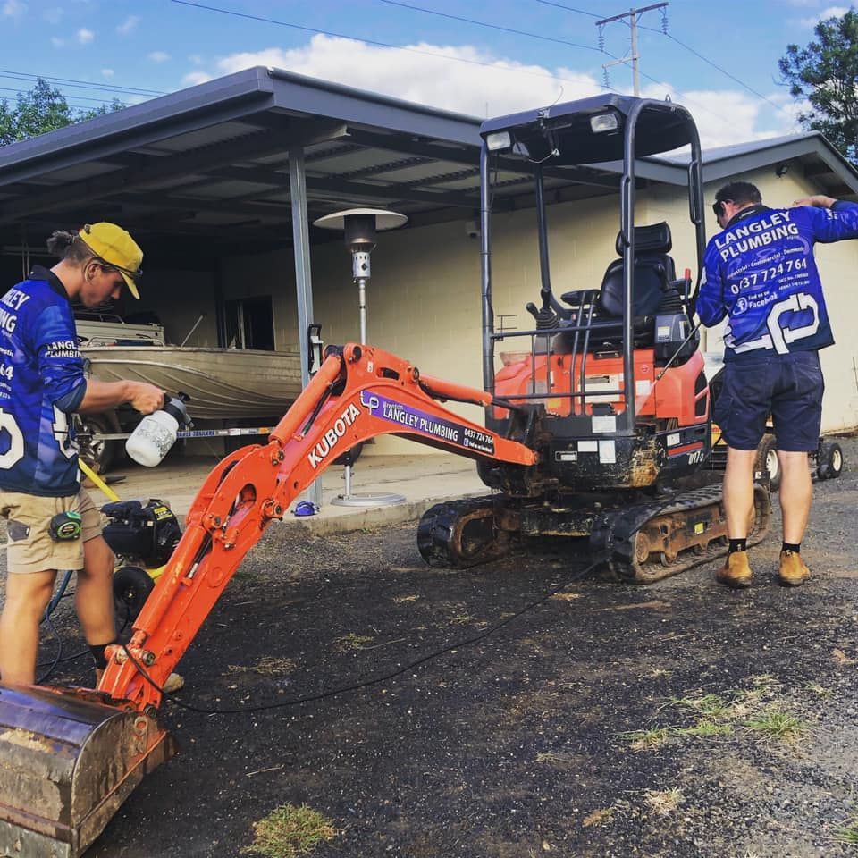 Two People Cleaning a Small Orange Kubota Excavator — Langley Plumbing in Mareeba, QLD