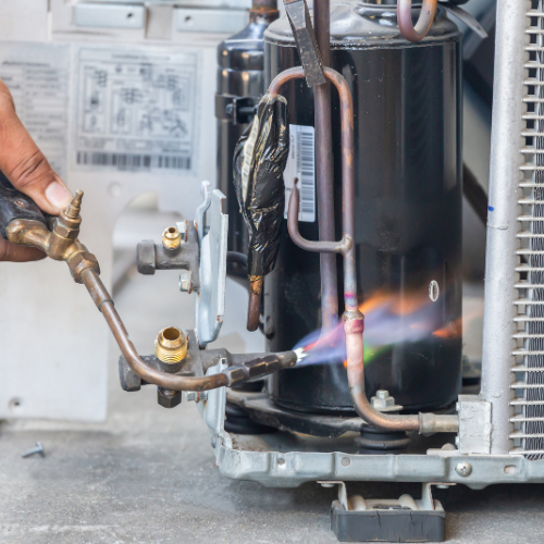 A person is working on an air conditioner with a torch
