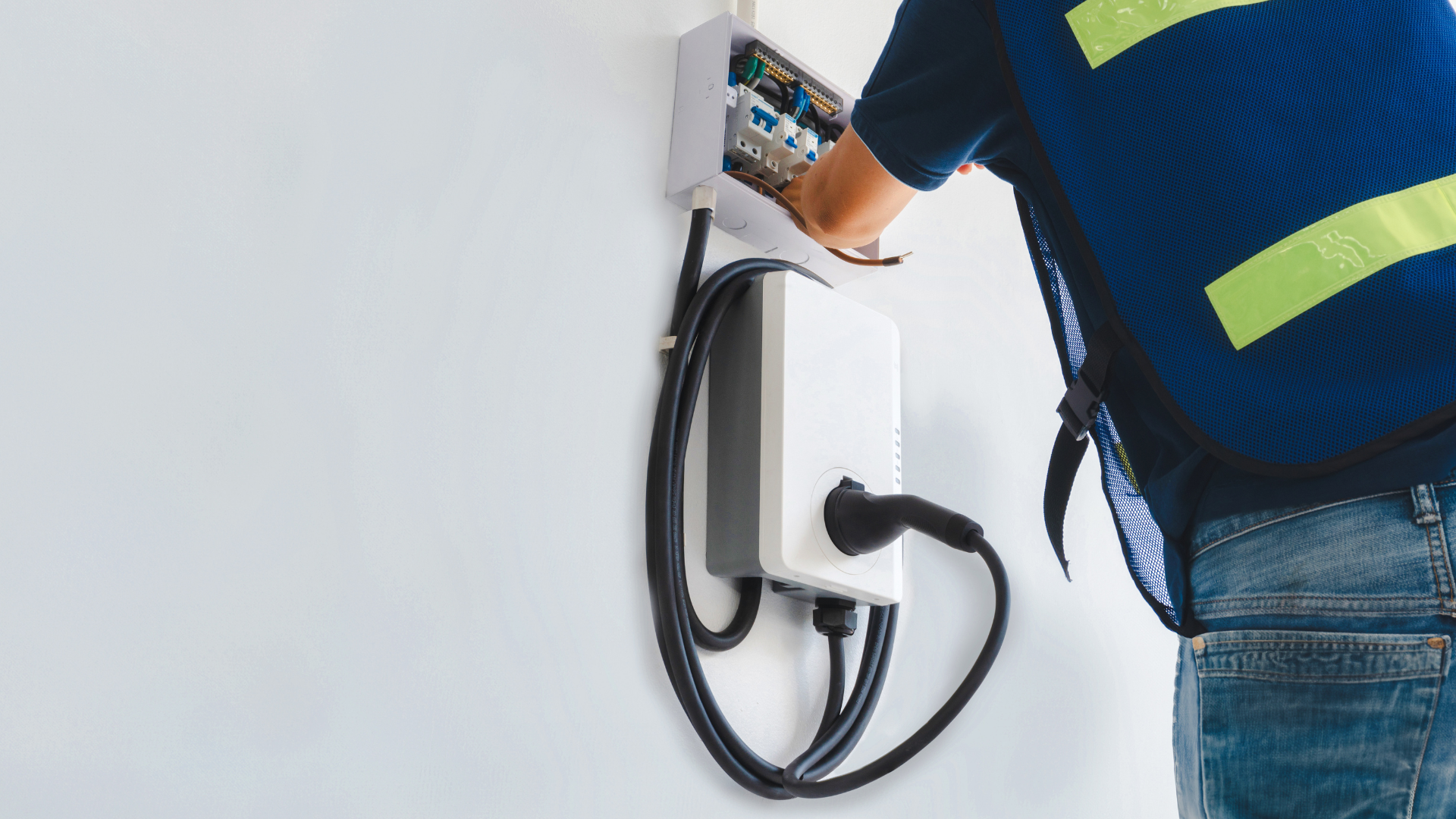 A man is installing an electric car charger on a wall.