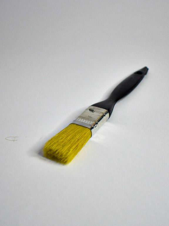 Pincel amarillo con mango negro sobre fondo blanco.