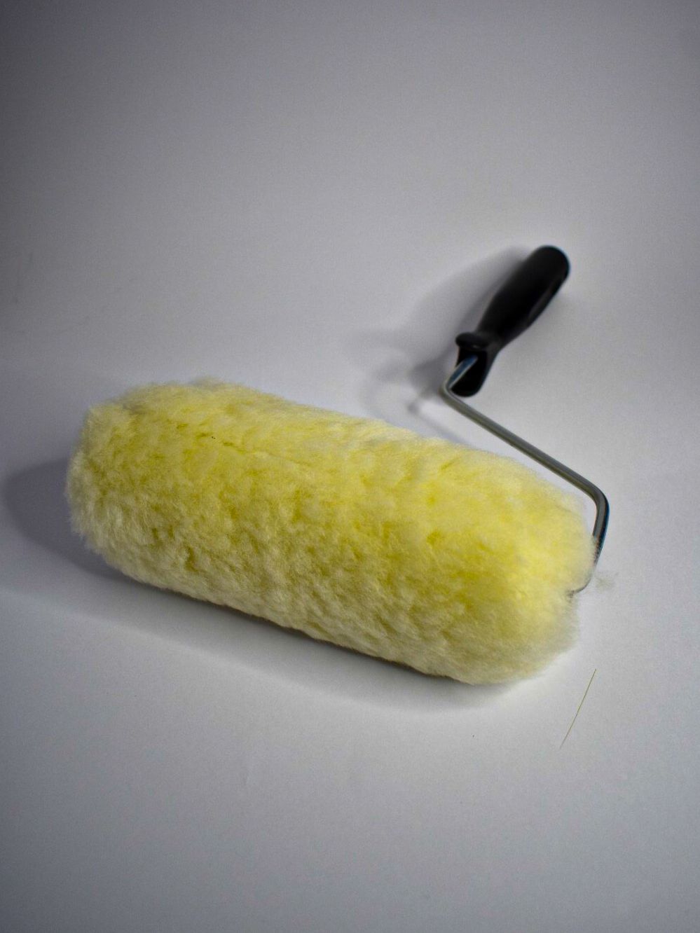 Rodillo de pintura amarillo con mango negro sobre fondo blanco.