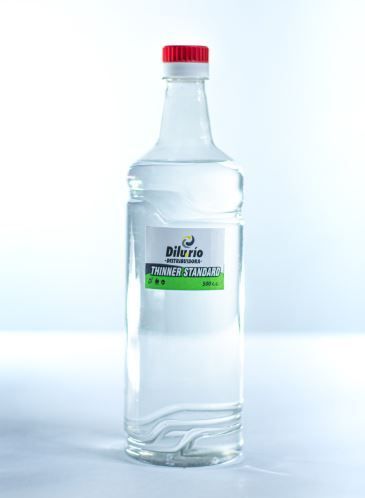 Botella de líquido de vidrio transparente, con etiqueta verde y blanca y tapón rojo, sobre fondo blanco.