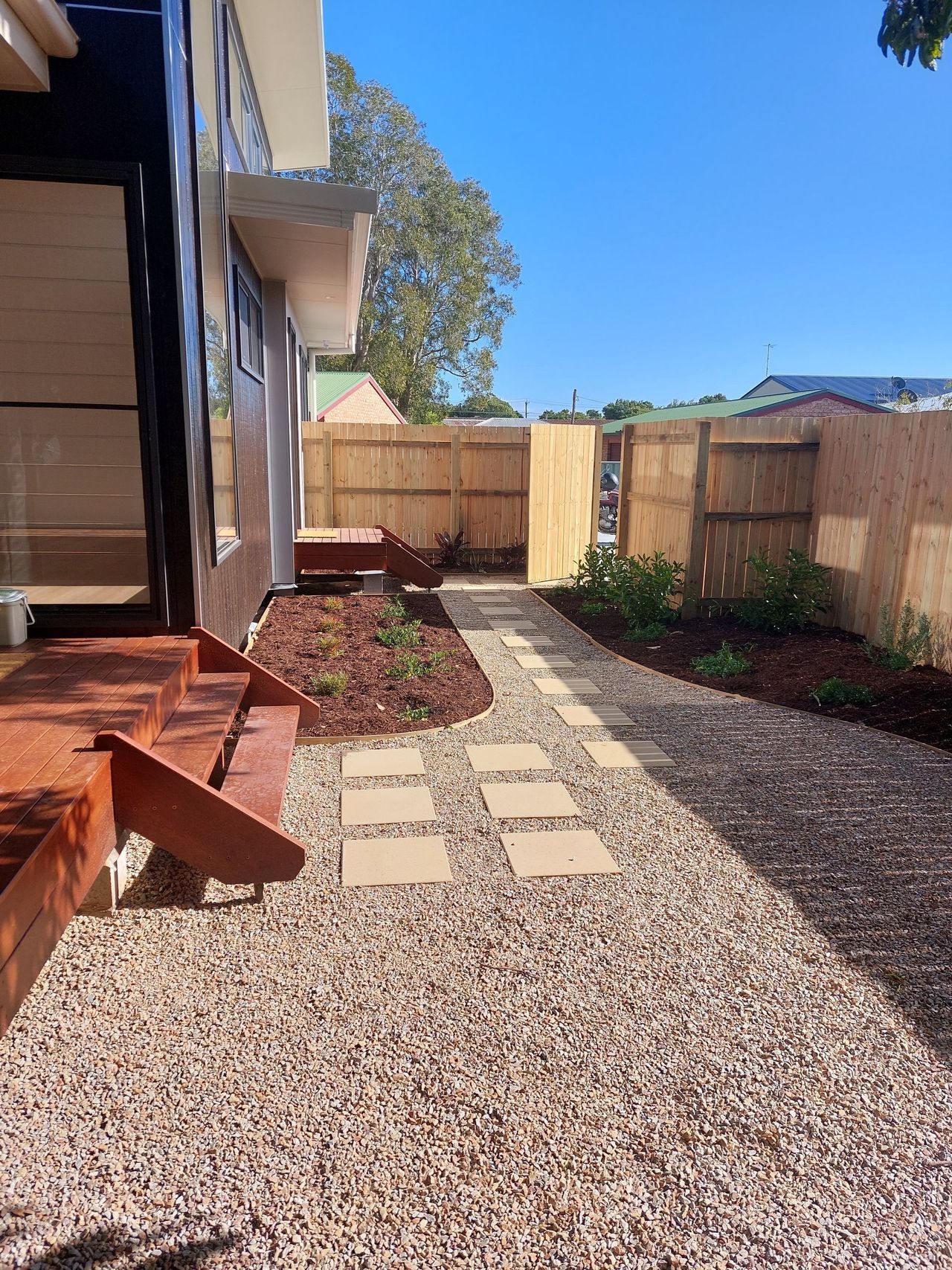 A gravel path leading to a house with a wooden fence.