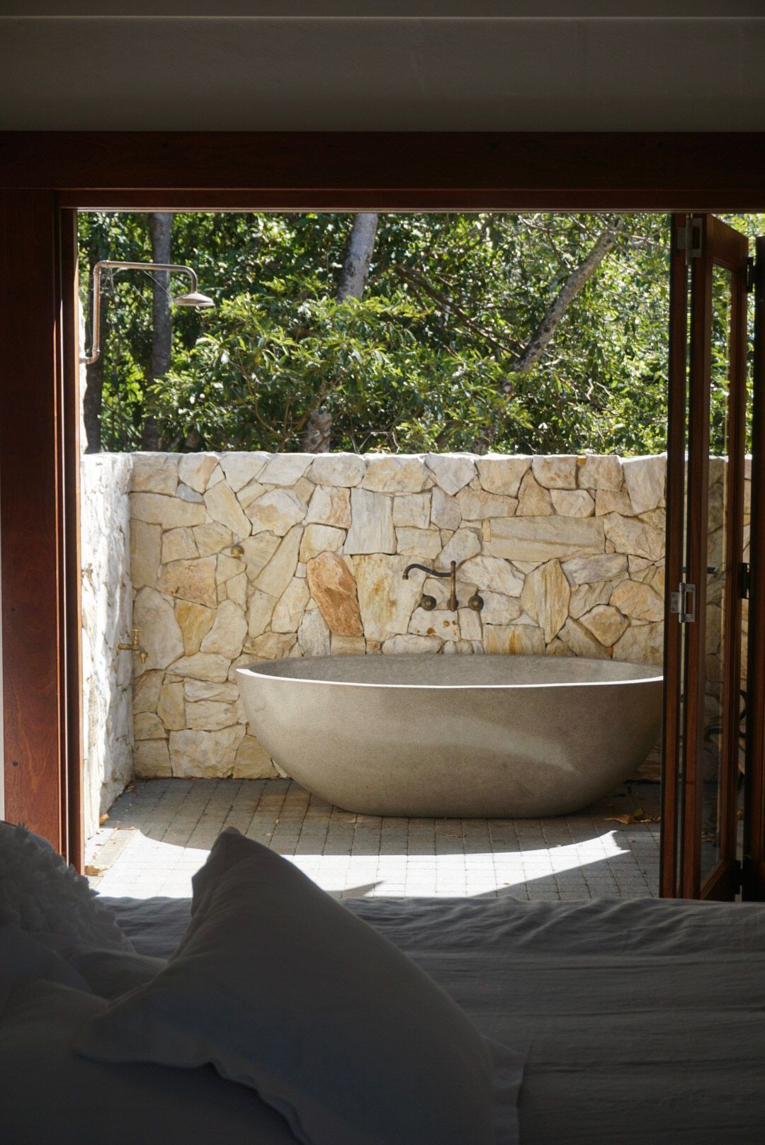 A bathtub is sitting outside of a bedroom next to a stone wall.