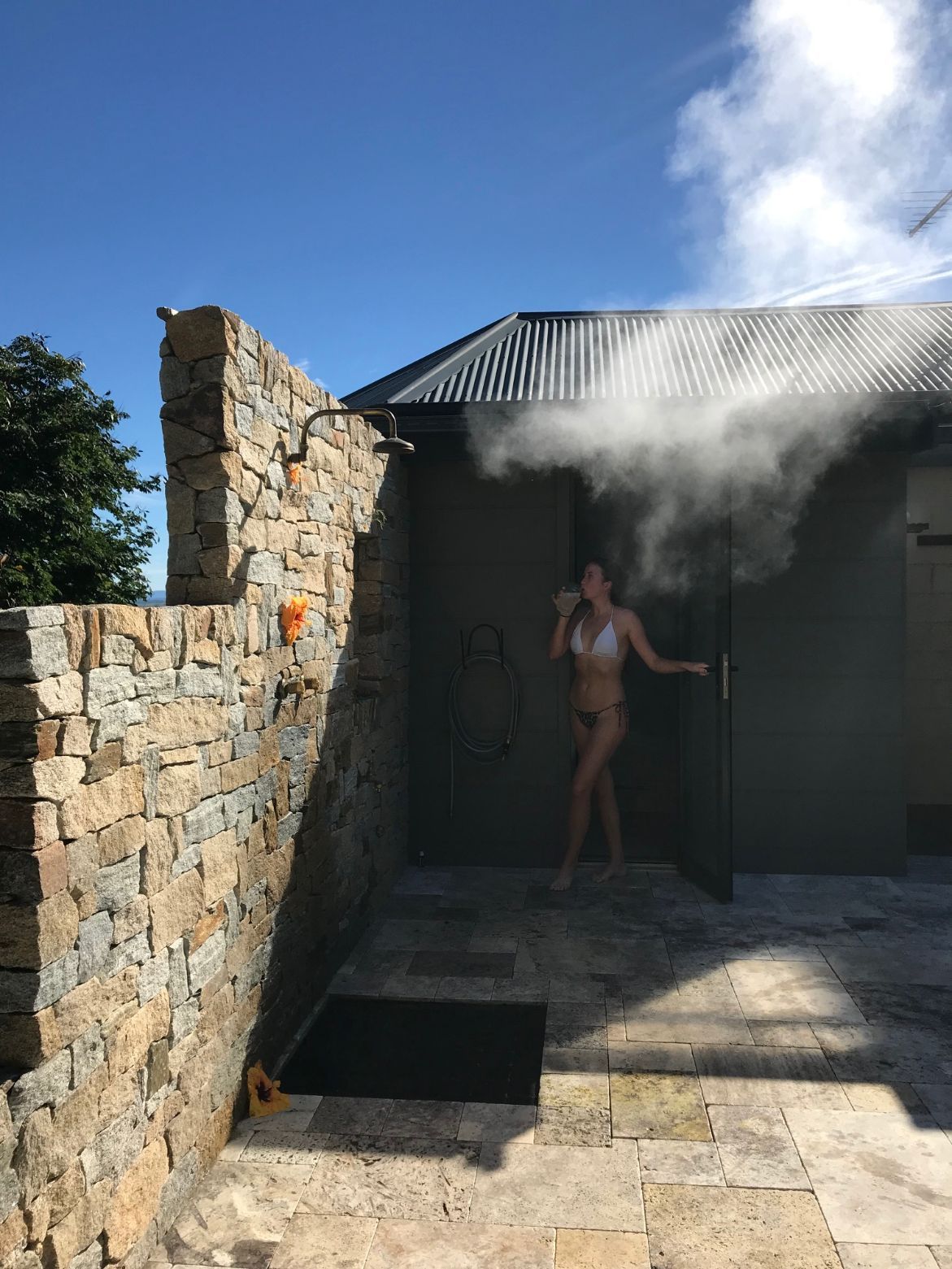 A woman in a bikini is taking a shower outside of a building.