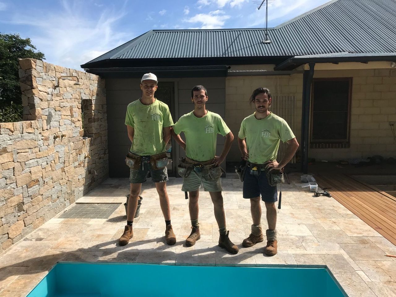 Three men are standing next to a pool in front of a house.