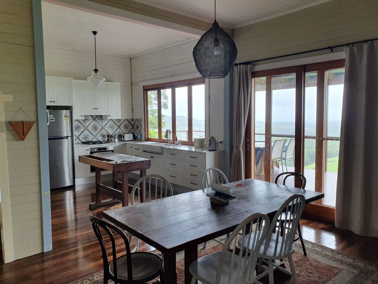 A dining room with a table and chairs and a kitchen in the background.
