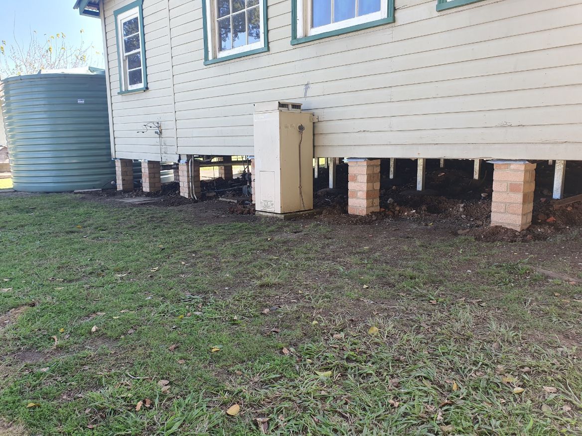 A house is sitting on stilts in the grass next to a water tank.
