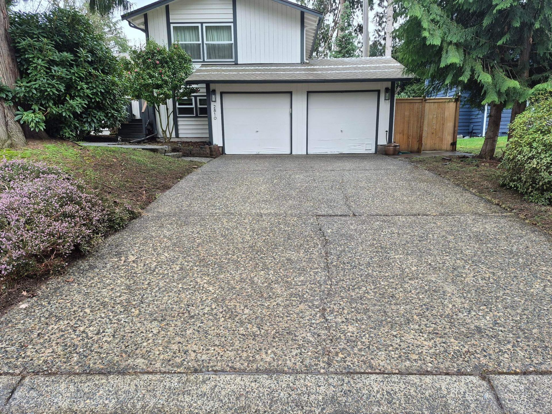Gravel driveway leading to a two-car garage with a house and trees in the background