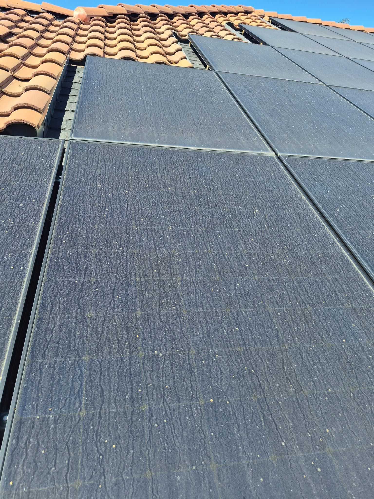 Roof with dark gray solar panels next to terracotta clay tiles under a sunny sky.