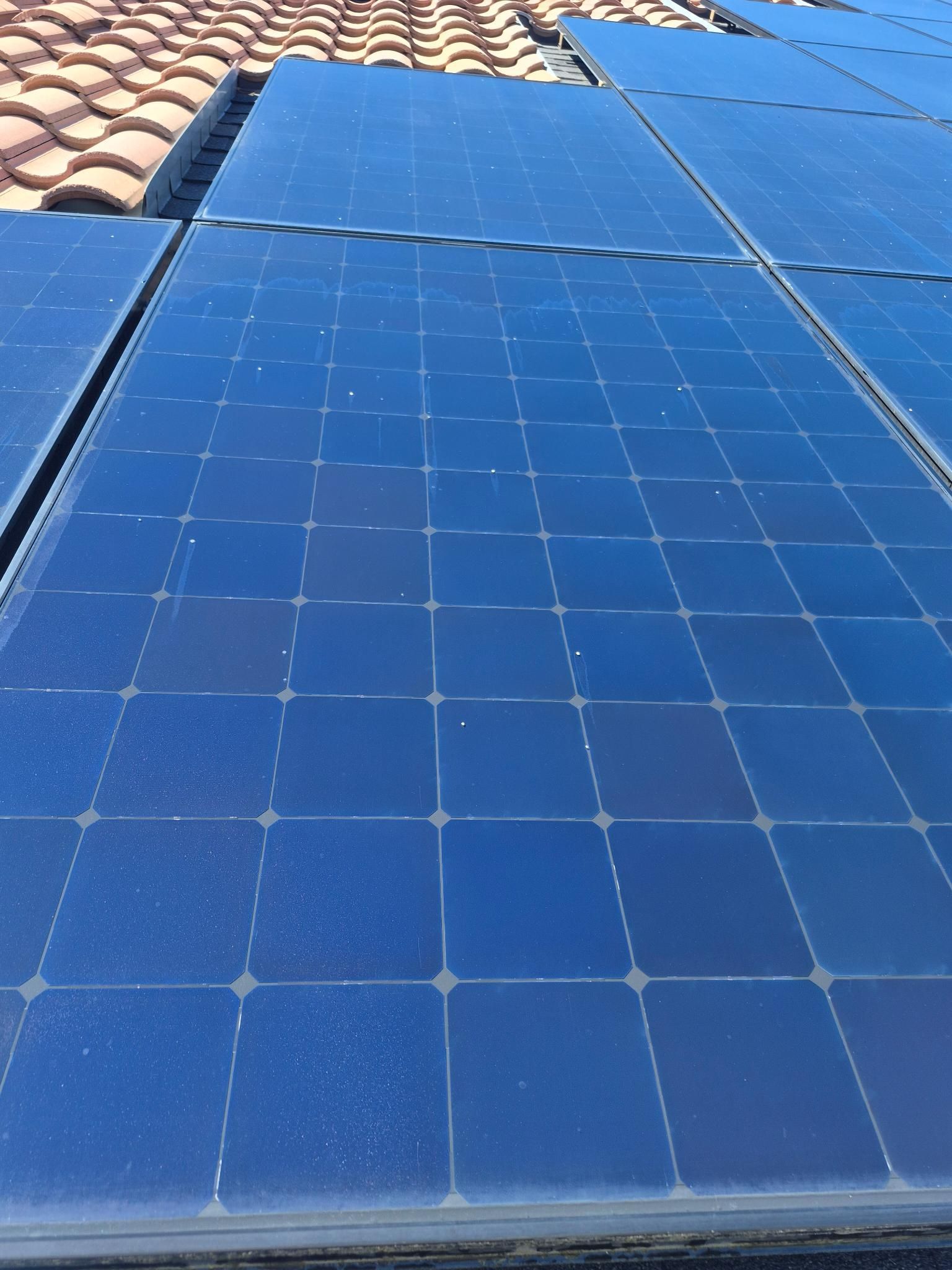Blue solar panels on a tiled rooftop under bright sunlight.