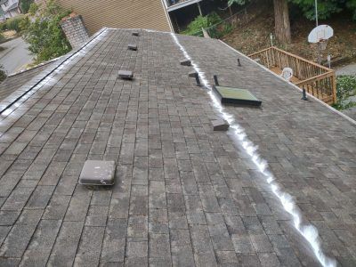 Damaged shingled roof with white roof sealant along a ridge and several vent boxes.