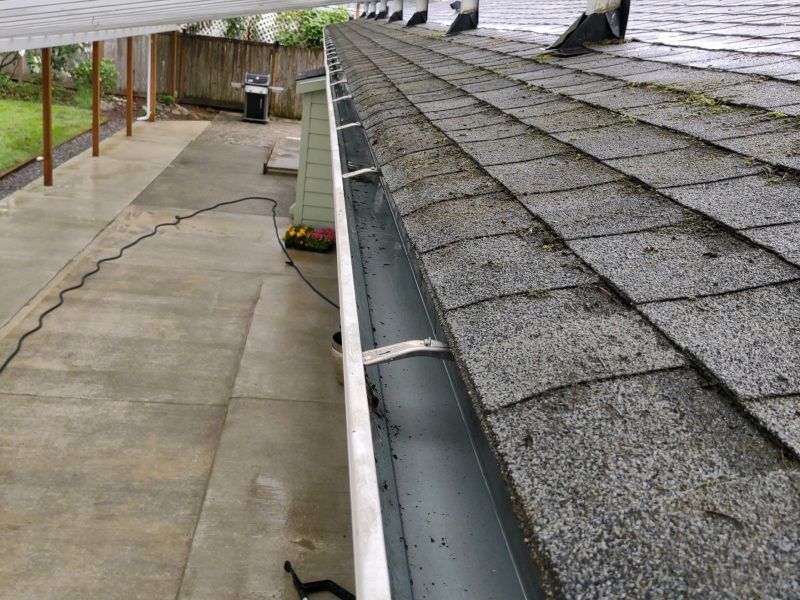 Roof shingles and a gutter beside a paved walkway under a covered patio.