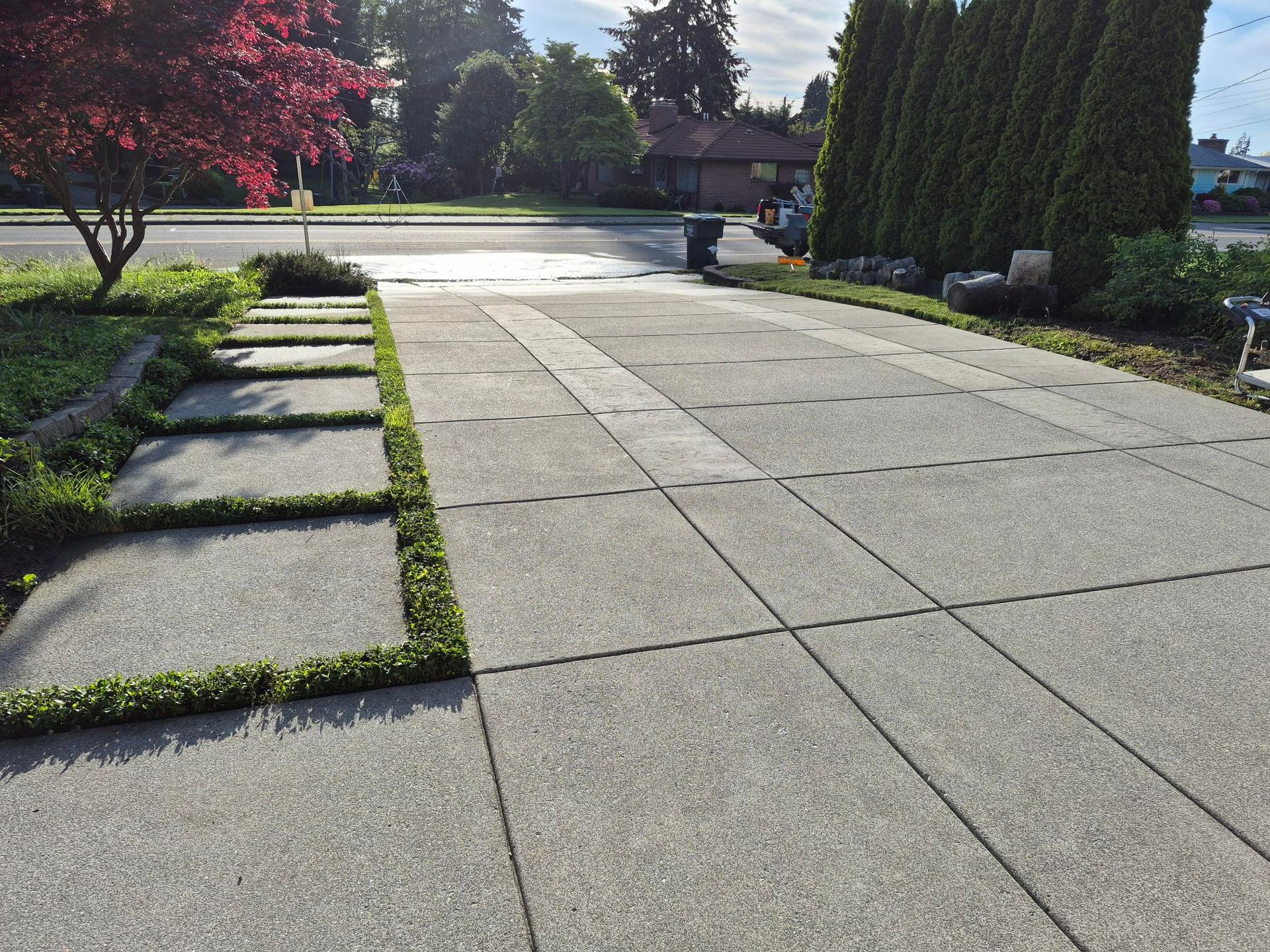 Stone walkway beside manicured garden beds and tall hedges in bright sunlight