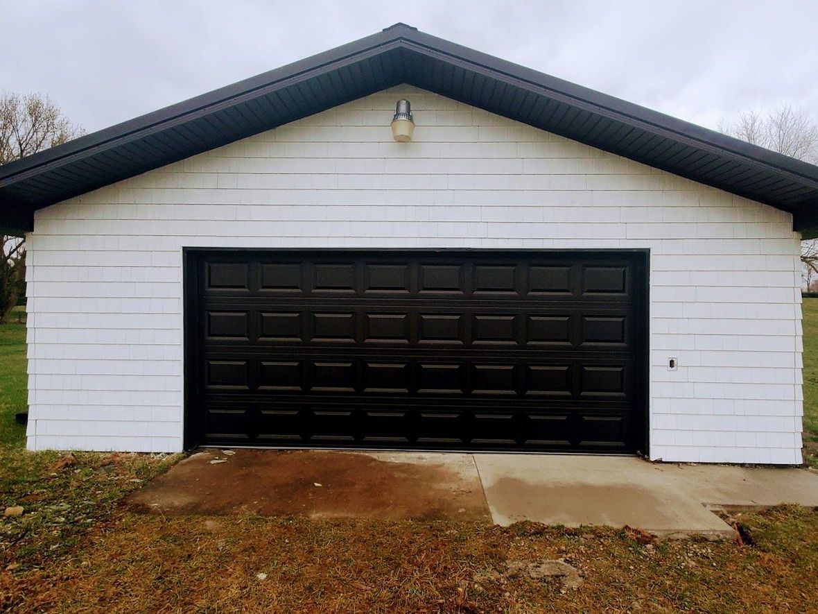 A white garage with a black garage door and a black roof.