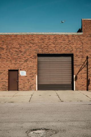 A brick building with a garage door and a drone flying overhead.