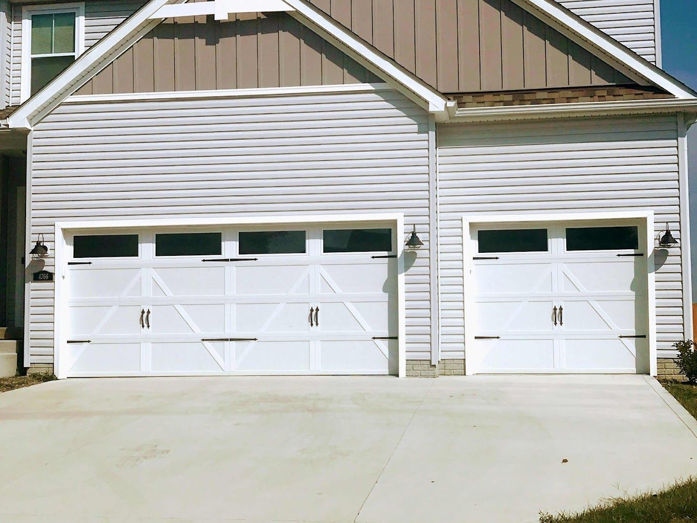 A house with two white garage doors and a concrete driveway.