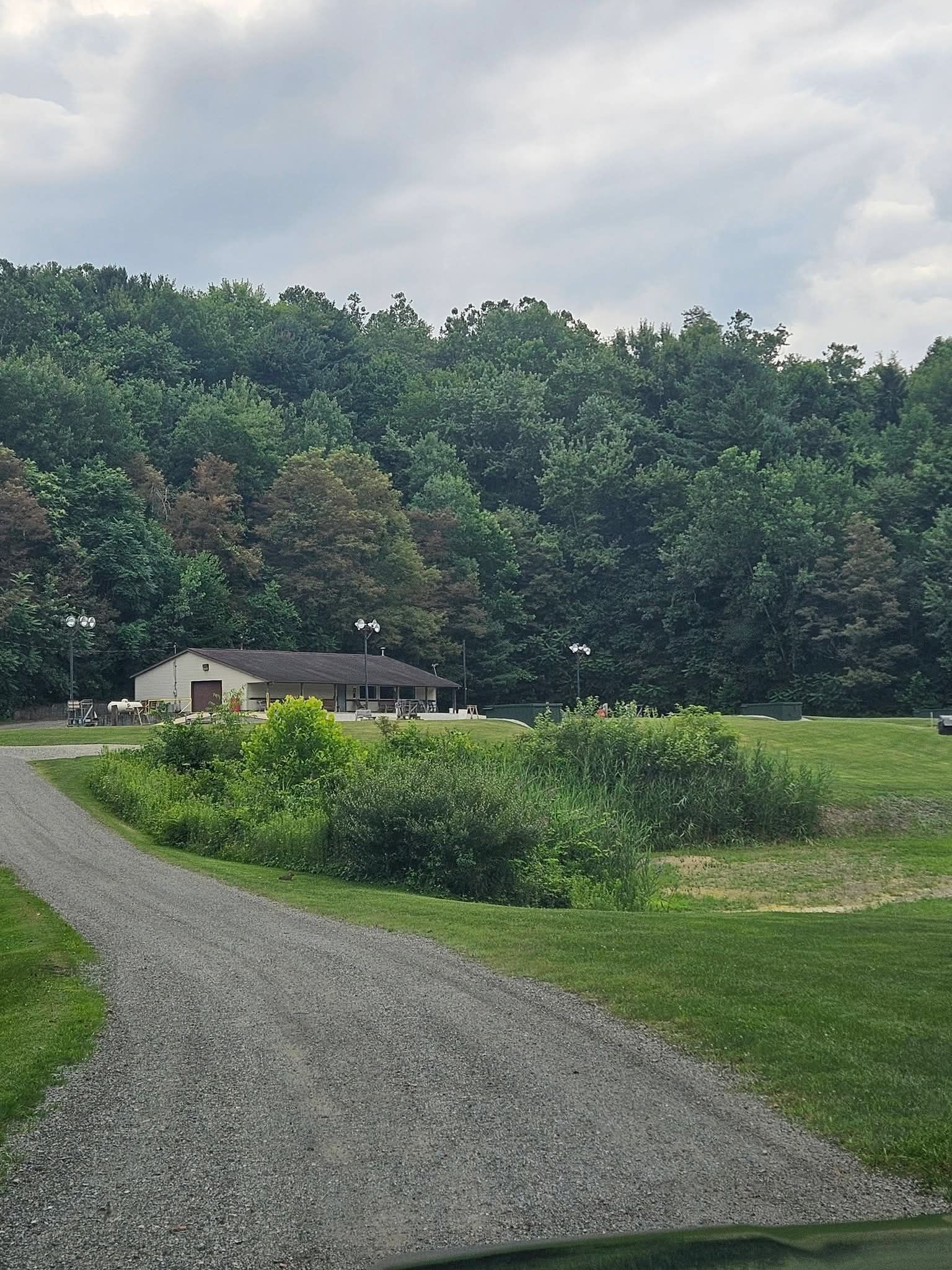 Gravel path leading to a small house beside a grassy field and dense trees under a cloudy sky