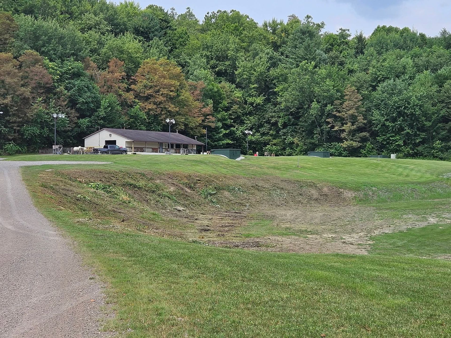 Rural house beside a gravel road, with green fields and dense trees in the background