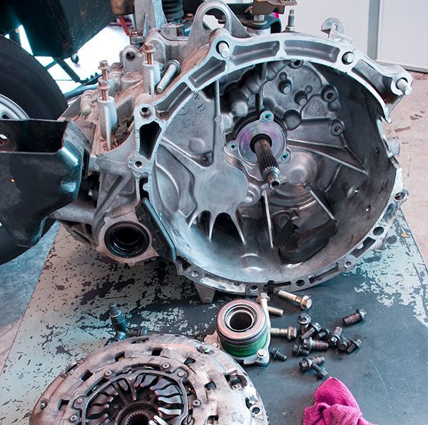 Disassembled car transmission on a workshop floor with clutch parts and bolts scattered nearby