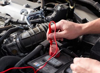 Person using red test leads to check a car engine battery compartment
