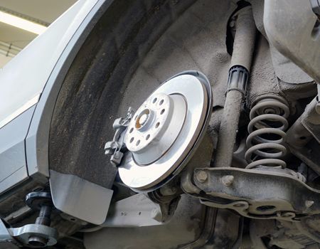 Car wheel hub and brake rotor exposed under raised vehicle, with suspension visible