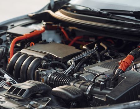 Car engine bay with black components and red wiring under an open hood