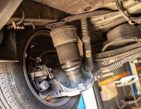 Undercarriage of a vehicle showing suspension, exhaust piping, and a rear wheel in a garage