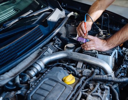 Mechanic using a multimeter to test wiring in a car engine bay