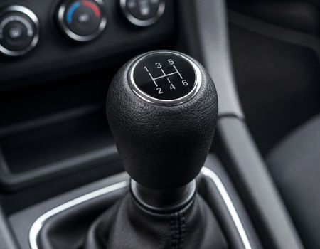 Close-up of a manual car gear shift knob with shift pattern in a dark interior.