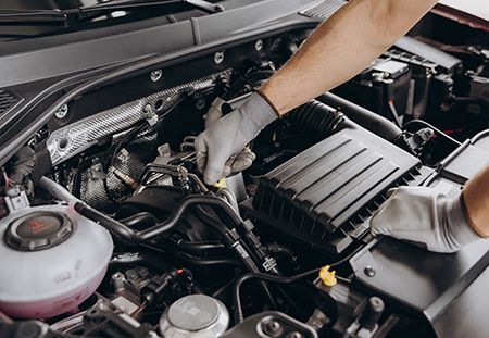 Mechanic working under a car hood with tools in an engine bay