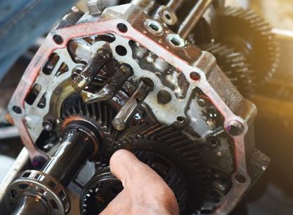 Close-up of a mechanic working on a car transmission with exposed gears and parts